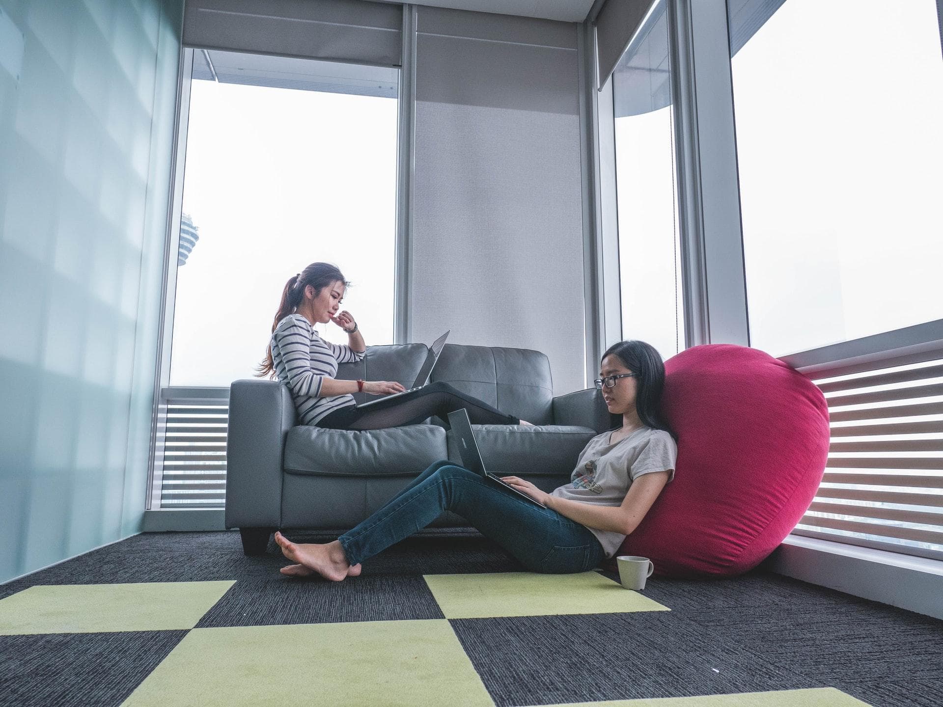 two girls sitting on a couch, typing on macBooks, looking concentrated